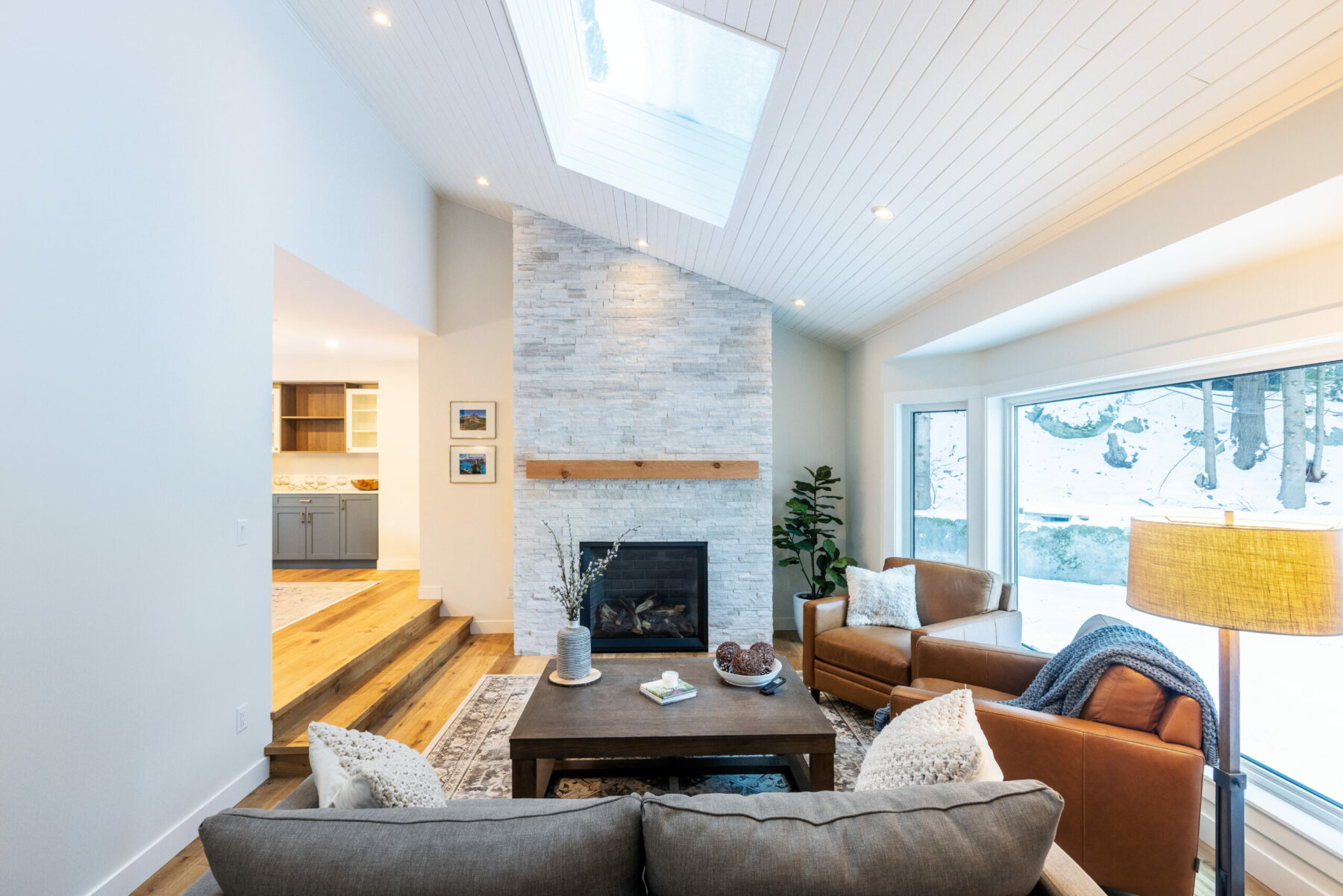 Living room at Blue Water Concepts’ Greenwood Way renovation, with a stone fireplace, wood floors and large windows.